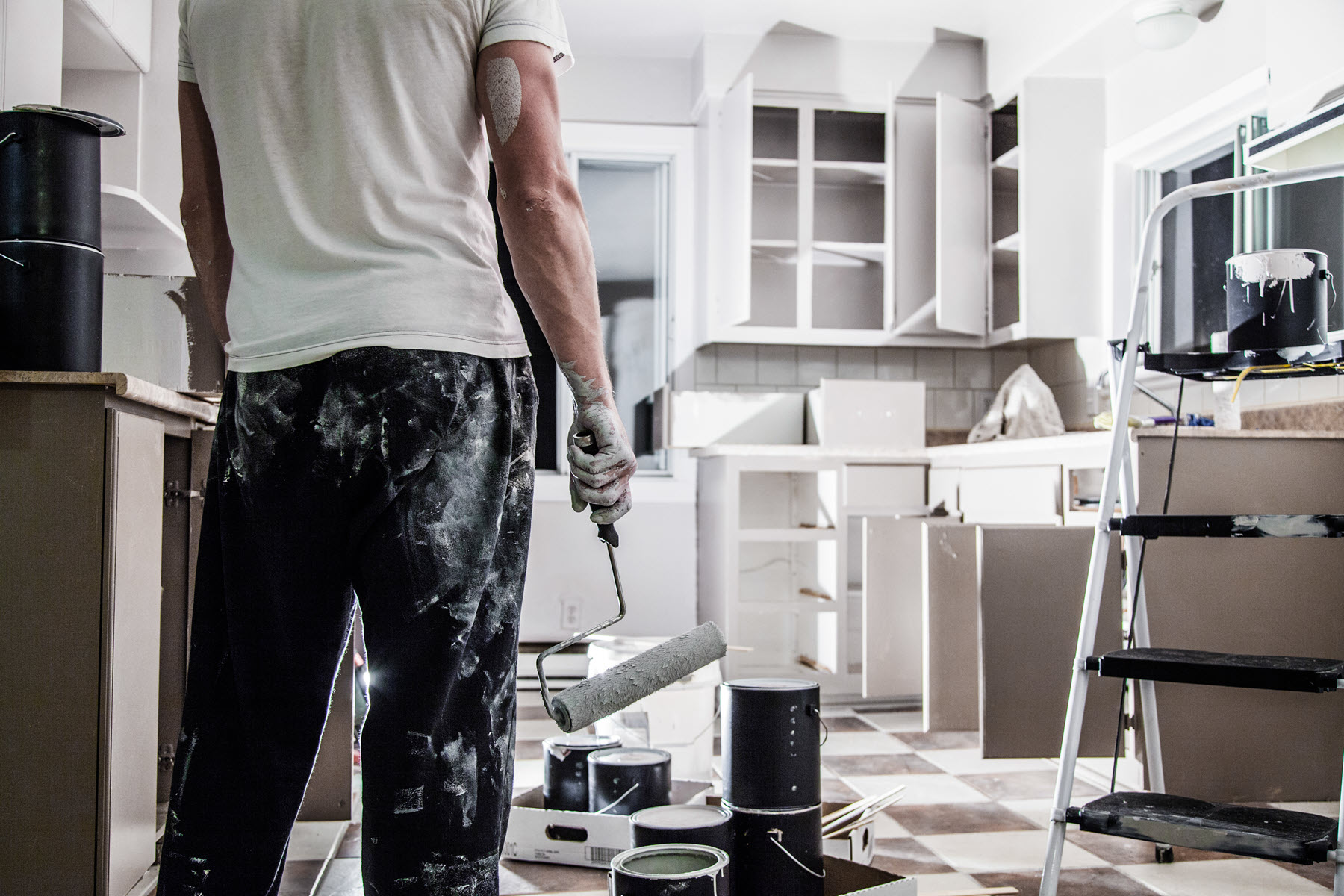 A man is renovating a kitchen with a paint roller.